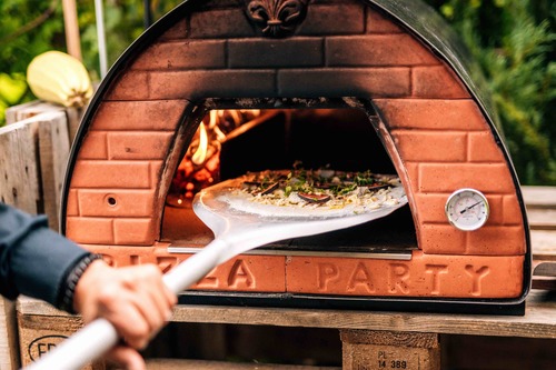 Domowa pizza pieczona a ogrodowym mobilnym piecu do pizzy opalanym drewnem